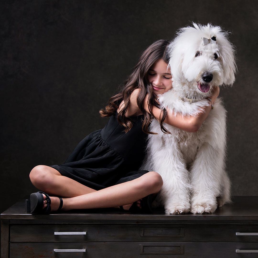 A girl sitting with her arms around a white Old English Sheepdog
